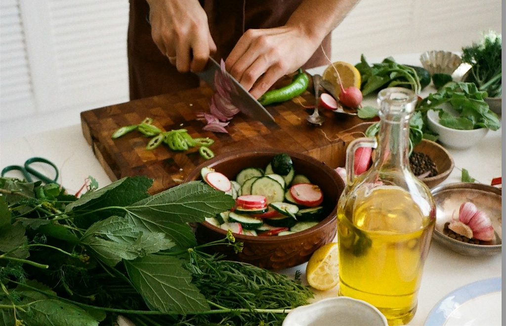 someone using a chef's knife prepares a variety of vegetables and leafy greens at a kitchen counter